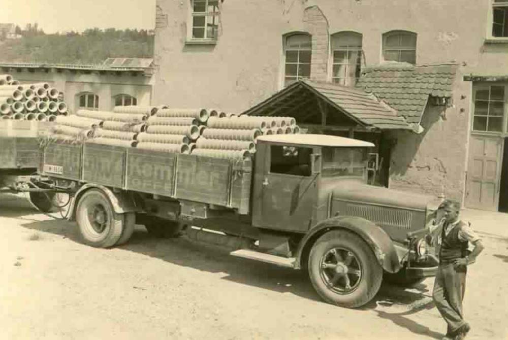 Lastwagen voller Betonrohre: Kemmler Geschichte der Erweiterung mit neuen Anlagen und erstem Lkw – erleichterter Transport und wachsender Absatzmarkt; Kemmler Tradition, Familiengeschichte Kemmler, Entstehung Firmen-Familie Kemmler.